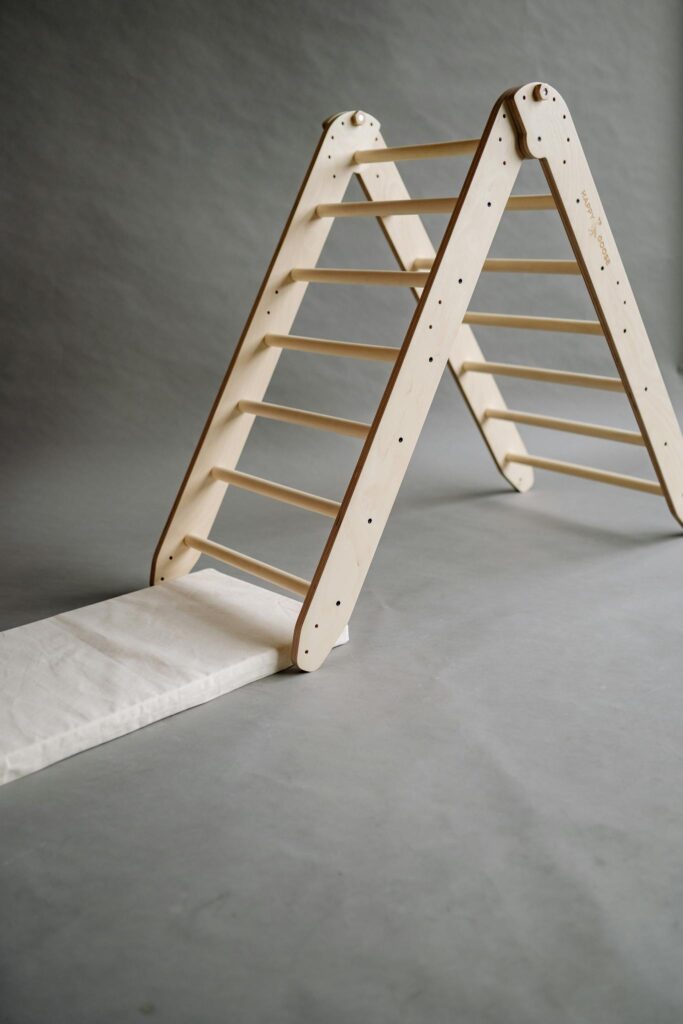 A minimalist wooden toy ladder against a gray playroom background.